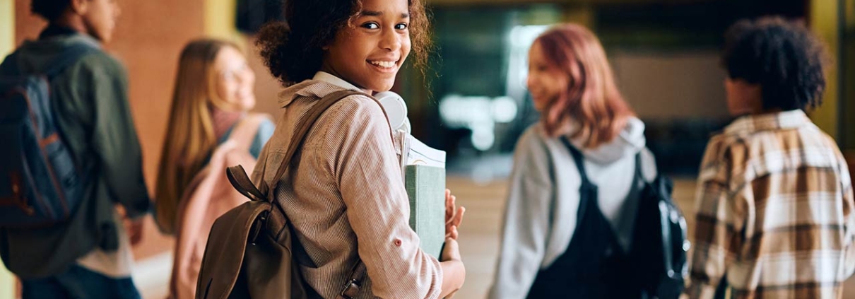 Happy African American high school student walking through hallway with her friends and looking at camera