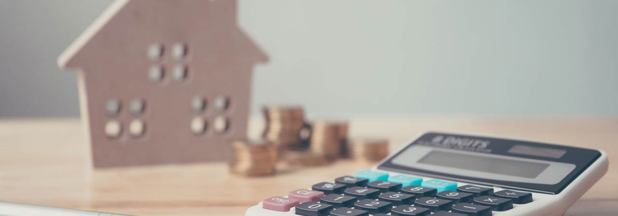 Calculator with wooden house and coins stack and pen on wood table