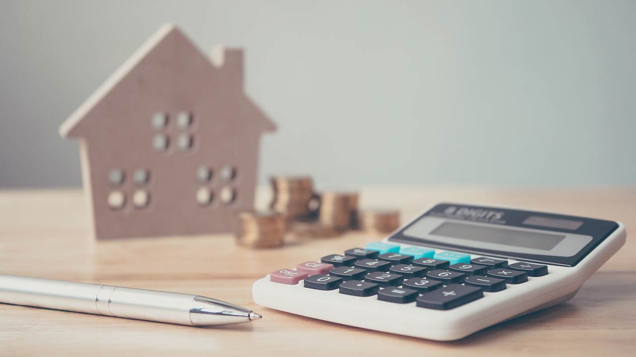 Calculator with wooden house and coins stack and pen on wood table