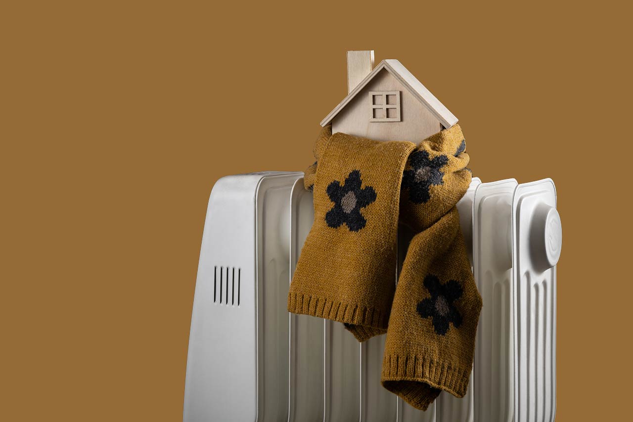 Wrapped in a warm scarf, a symbolic wooden house stands on an electric radiator