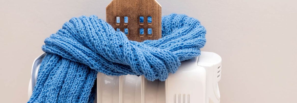 Wooden model house wrapped in a blue scarf on a radiator